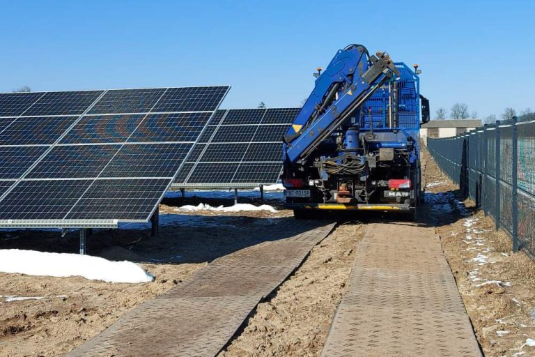 Ciężarówka z podnośnikiem stoi obok paneli słonecznych na terenie wykorzystywanym do energii odnawialnej.