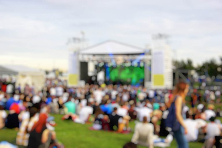 Tłum ludzi siedzących na trawie przed sceną na wydarzeniu plenerowym.