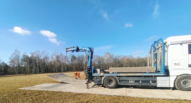 Ciężarówka z dźwigiem na placu budowy, pracownicy przygotowujący teren w słoneczny dzień.