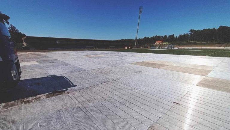 Widok na boisko sportowe pokryte dużymi, jasnymi płytami, z niebieskim niebem w tle.