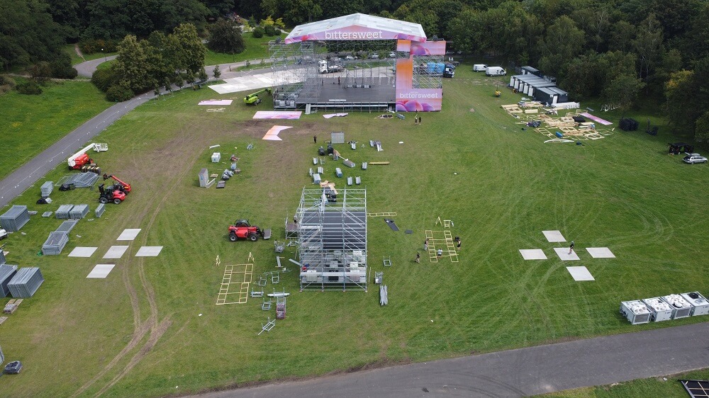 Budowa sceny plenerowej z różowym frontem, rusztowaniami i pojazdami na trawie