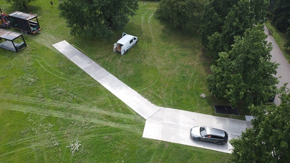 Widok z góry: tymczasowa metalowa droga przez trawnik, samochód i biała furgonetka