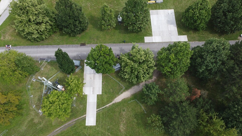 Widok z lotu ptaka na park z alejką, betonowymi podestami i skupiskami drzew