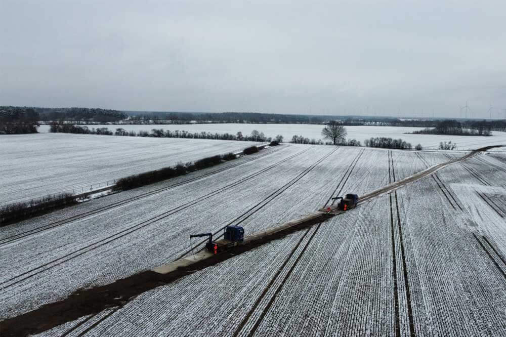Widok na zimowe pole pokryte śniegiem, z dwiema maszynami na drodze w centralnej części obrazu.