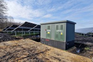 Zespół paneli słonecznych na tle nieba oraz stacja transformacyjna na działce.