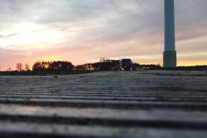 Widok na drogę z bliskiej perspektywy, w tle zachód słońca, na horyzoncie ciągnik i wiatrak.