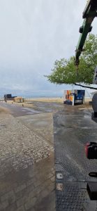 Widok na plażę z przyczepą, metalową konstrukcją i drzewem w tle, w pochmurny dzień.