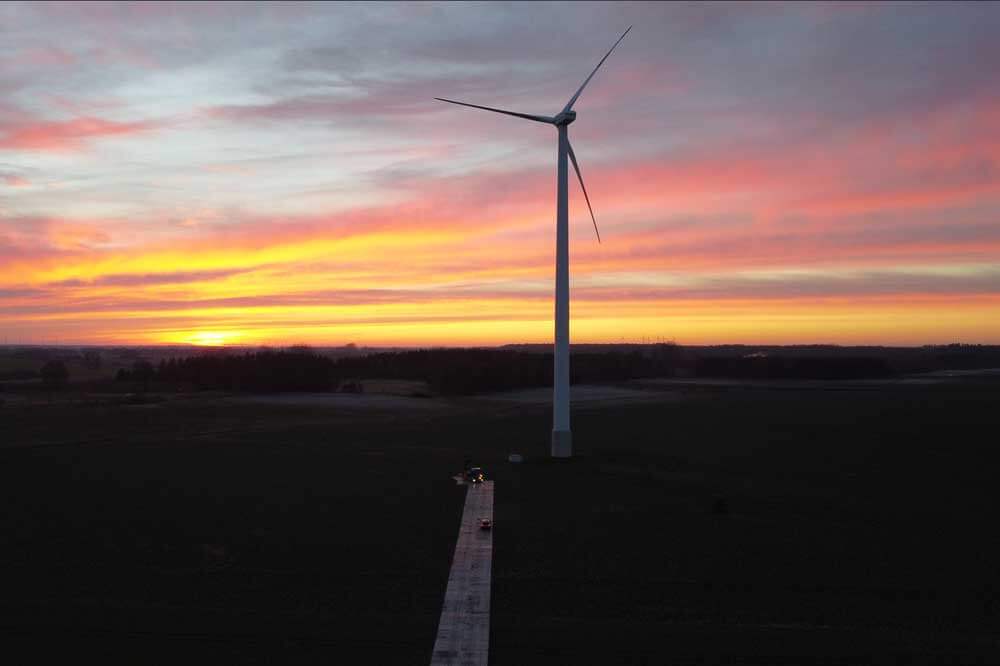 Wiatrak na zielonym polu podczas zachodu słońca. Kolorowe chmury na niebie tworzą malowniczy widok.