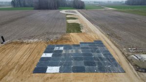 Widok z lotu ptaka na pole z ułożonymi płytami na nawierzchni drogi i otaczającymi uprawami.