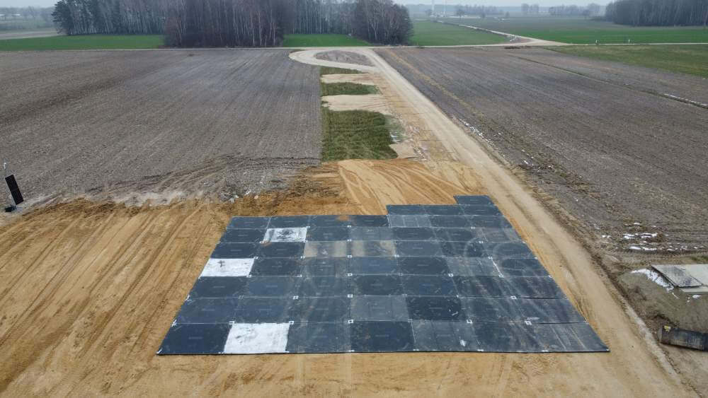 Widok z lotu ptaka na pole z ułożonymi płytami na nawierzchni drogi i otaczającymi uprawami.