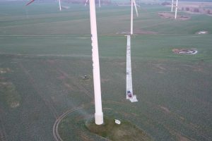 Widok na pola z wieżami wiatrowymi, w tle zielona trawa, z małym obszarem betonowym na ziemi.