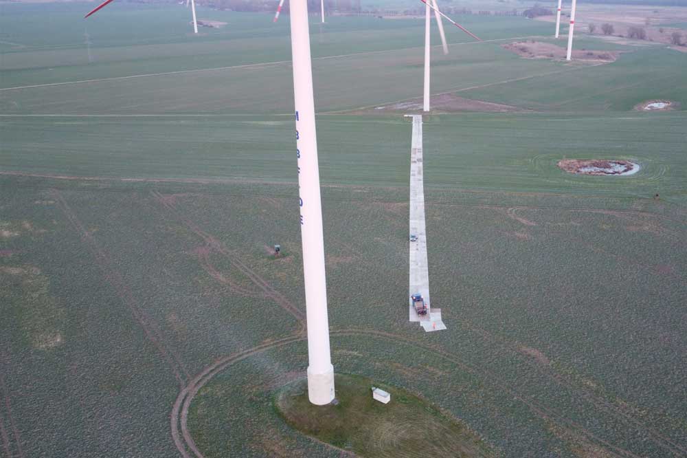 Widok na pola z wieżami wiatrowymi, w tle zielona trawa, z małym obszarem betonowym na ziemi.