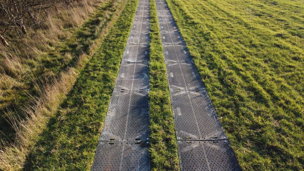 Dwujezdniowa droga z metalowymi panelami, otoczona zielonym trawnikiem i łagodnymi brzegami.