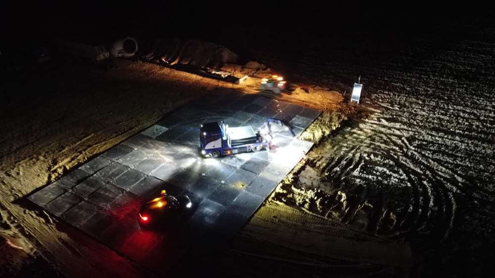 Prace budowlane w nocy na placu budowy, oświetlona maszyna i pojazdy na działce z ziemią.