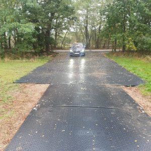 Na zdjęciu widać samochód na czarnej, gumowej nawierzchni, otoczony drzewami i krzewami w lesie.