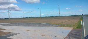 Rozległe pola z widokiem na wiatraki na tle nieba z chmurami. Blisko asfaltowa droga.