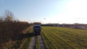 Samochód ciężarowy stoi na polu, w tle widać drzewa i inne pojazdy, niebo jest jasne i częściowo pochmurne.