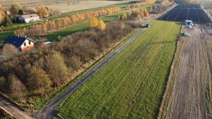 Widok z góry na teren wiejski z domami, pola, drzewa i niewielką farmę paneli słonecznych.