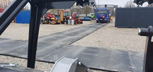 Na obrazie widać plac z maszynami budowlanymi, w tym ciągnikami i ciężarówką na drodze z metalowych płyt.