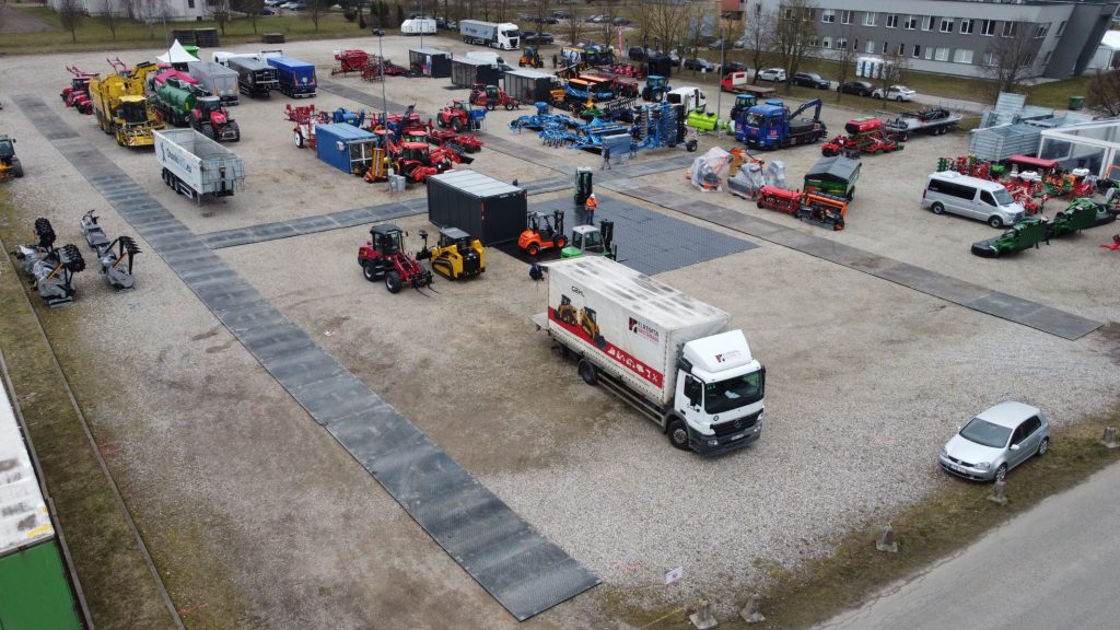 Park maszynowy z różnorodnym sprzętem rolniczym i budowlanym, samochodami dostawczymi i widocznymi alejkami.