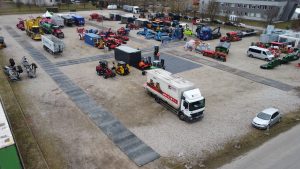 Park maszynowy z różnorodnym sprzętem rolniczym i budowlanym, samochodami dostawczymi i widocznymi alejkami.