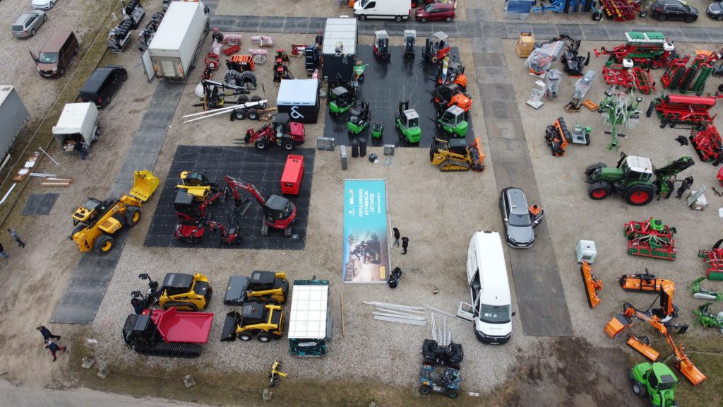 Widok z lotu ptaka na teren z urządzeniami rolniczymi i budowlanymi, w tym ciężkim sprzętem i pojazdami.