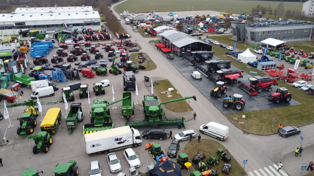 Widok z góry na targi rolnicze z różnorodnymi ciągnikami, maszynami i sprzętem. W tle budynki i parkowe tereny.