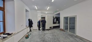 Dwaj mężczyźni stoją przy maszynie w nowoczesnym, jasnym pomieszczeniu. Na podłodze widoczny beton.