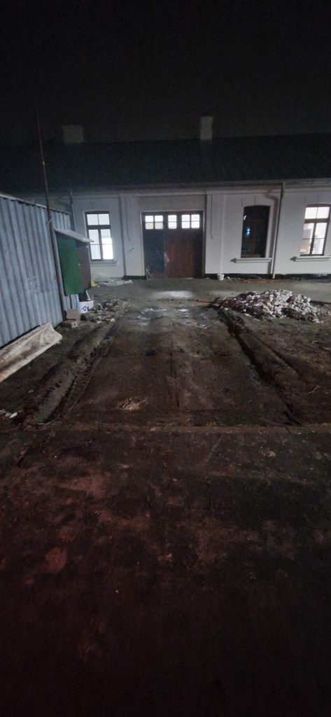 Widok na wyjazd z podwórza w nocy, z wąską ścieżką i budynkami po obu stronach.