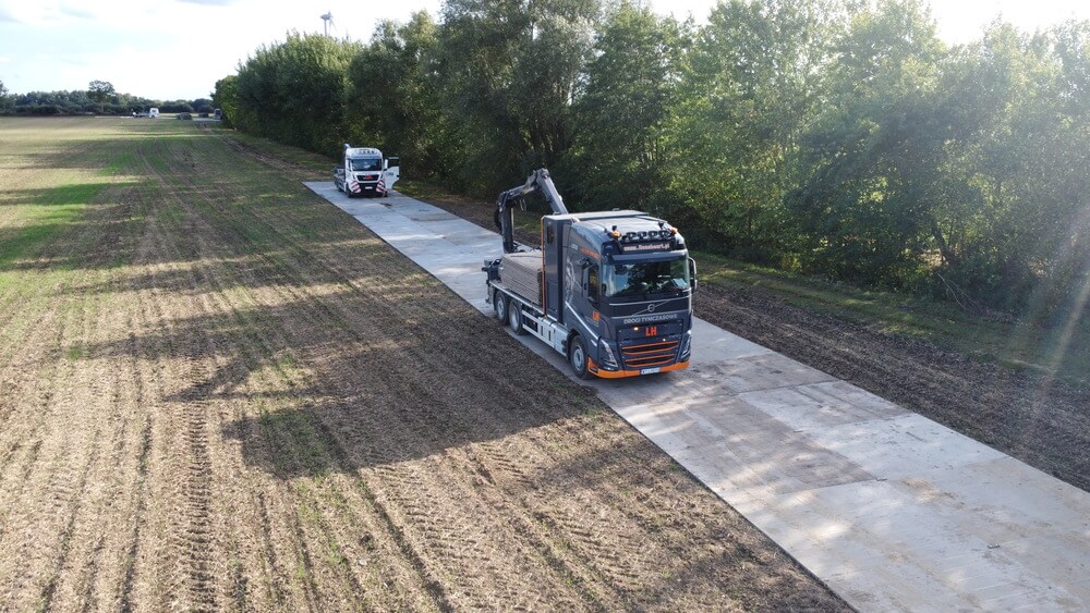 Dwa ciężarówki na polnej drodze, otoczone drzewami, jeden z pojazdów z wysięgnikiem.