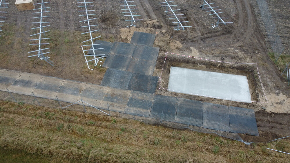 Ziemny teren z betonową podstawą i płytami, obok nieukończony parking dla pojazdów.