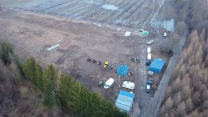 Widok na plac budowy z maszynami, materiałami budowlanymi i obszarem z panelami fotowoltaicznymi w tle.