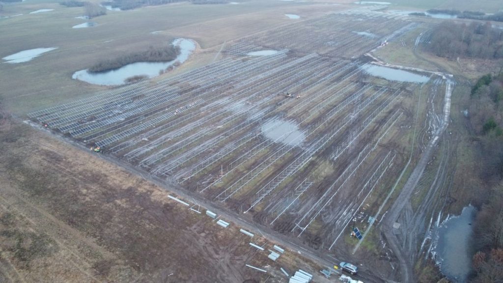 Widok z lotu ptaka na pole z panelami słonecznymi, otoczone wodami oraz błotnistymi powierzchniami.