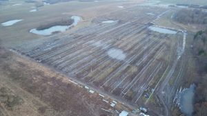 Widok z lotu ptaka na pole z panelami słonecznymi, otoczone wodami oraz błotnistymi powierzchniami.