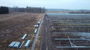 Widok na teren budowy instalacji, w tle widać puste pole, w prawej części rzędy konstrukcji pod panele słoneczne.