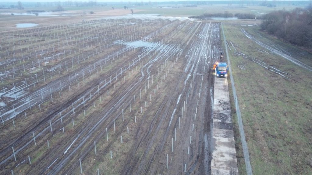 Widok z lotu ptaka na puste pola z rzędem młodych roślin, w tle samochód i błotnista droga.
