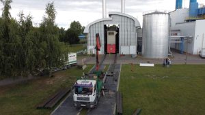 Na zdjęciu widać teren przemysłowy z ciężarówką oraz dużymi zbiornikami. Obok stoją ludzie, a w tle widać fabrykę.