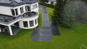 Widok na nowoczesny dom z dużymi oknami, chodnik z płyt i drzewa w otoczeniu.