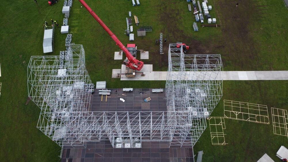 Widok z góry na plac budowy konstrukcji z metalowych stelaży, w tle widoczne maszyny budowlane.