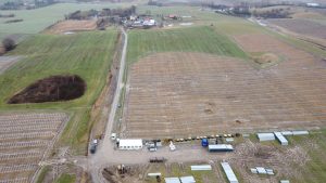 Widok z lotu ptaka na pola uprawne i infrastrukturę rolniczą, z sprzętem i budynkami w tle.