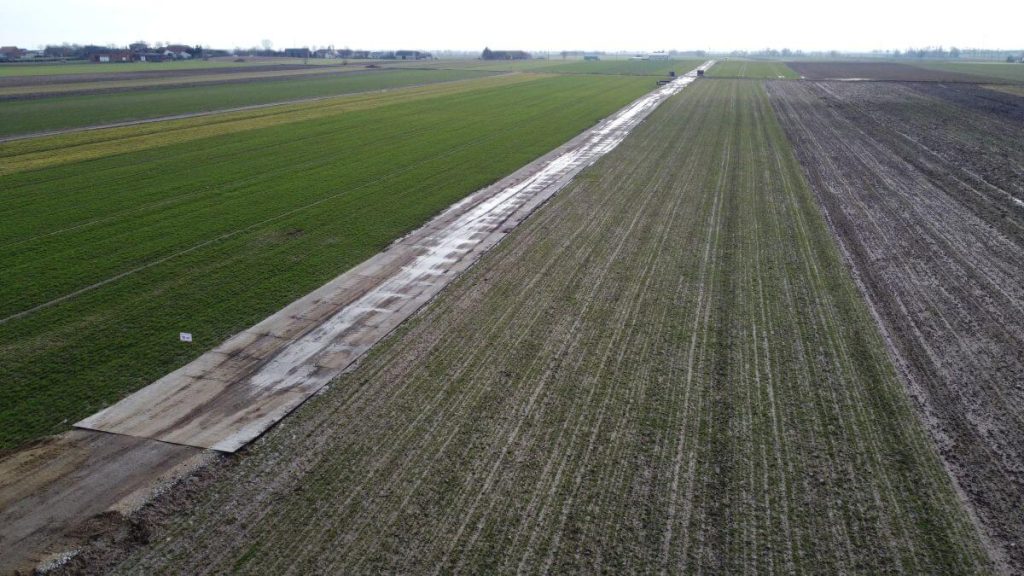 Obraz przedstawia szeroką, płaską działkę rolną podzieloną na obszary z różnymi rodzajami upraw.