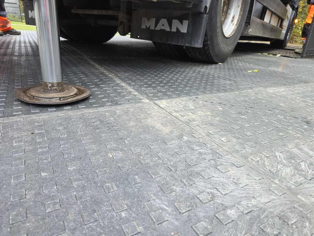 Widok na nawierzchnię z płyt gumowych, część ciężarówki MAN oraz stabilizator na ziemi.