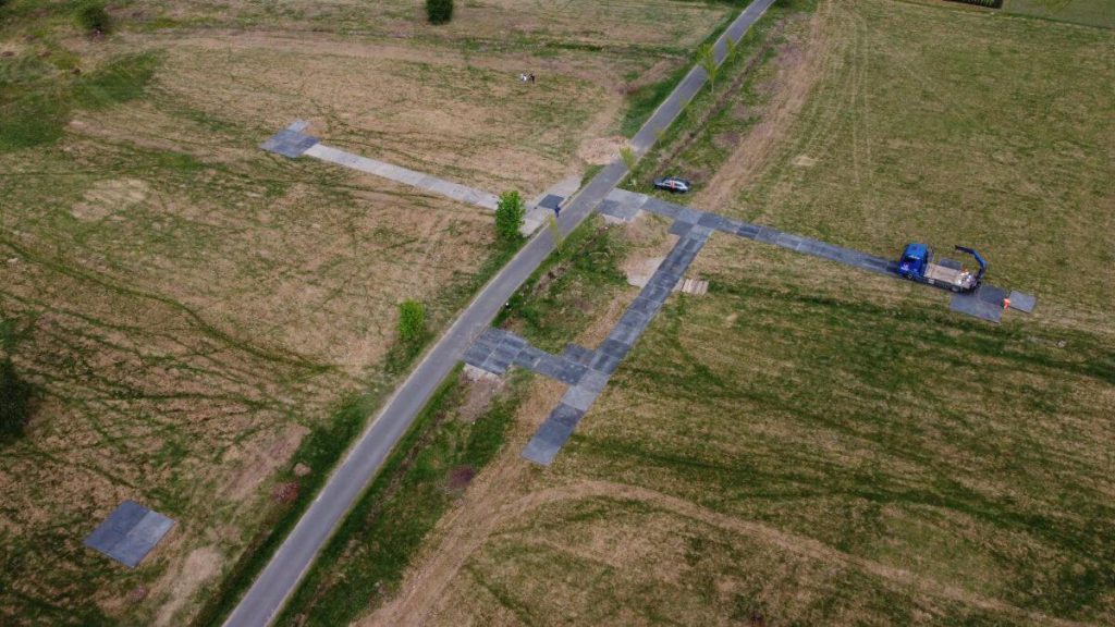 Widok lotniczy na krzyżujące się drogi w otwartym terenie, z maszyną budowlaną i niewielkimi drzewami.