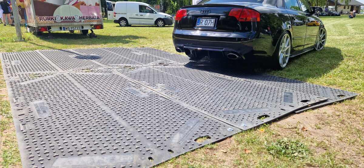 Czarny samochód osobowy marki Audi parkowany na gumowej matowej powierzchni na trawie.