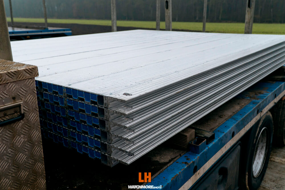 Stalowe panele leżą na platformie ciężarówki, w tle widać zielone pole i mglistą przestrzeń.