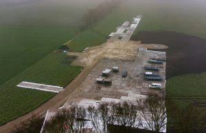 Widok na plac budowy z wyłożonym betonem, maszynami i terenami zielonymi otaczającymi obszar.