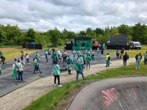Tłum kibiców w zielonych strojach na terenie imprezy, z plakatami i ekranem w tle. Zieleń drzew wokół.