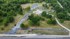 Widok z góry na park z alejkami, zielonymi drzewami oraz placem zabaw w centralnej części.