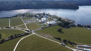 Widok z lotu ptaka na teren nad wodą z białymi namiotami, zielonymi polami i okalającą je rzeką.