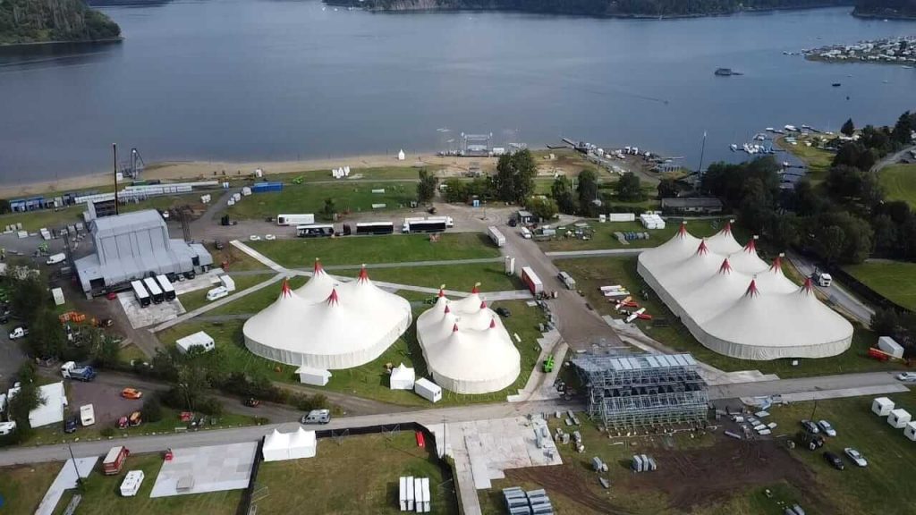 Widok na teren festiwalu z namiotami, wodą w tle oraz różnymi strukturami i pojazdami.